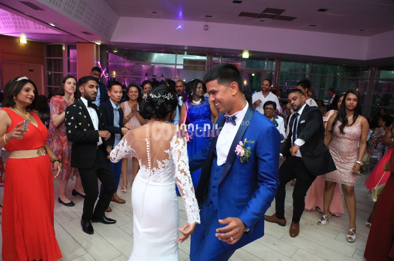 Un couple danse au centre d'une salle de réception entouré d'invités en tenue de soirée.