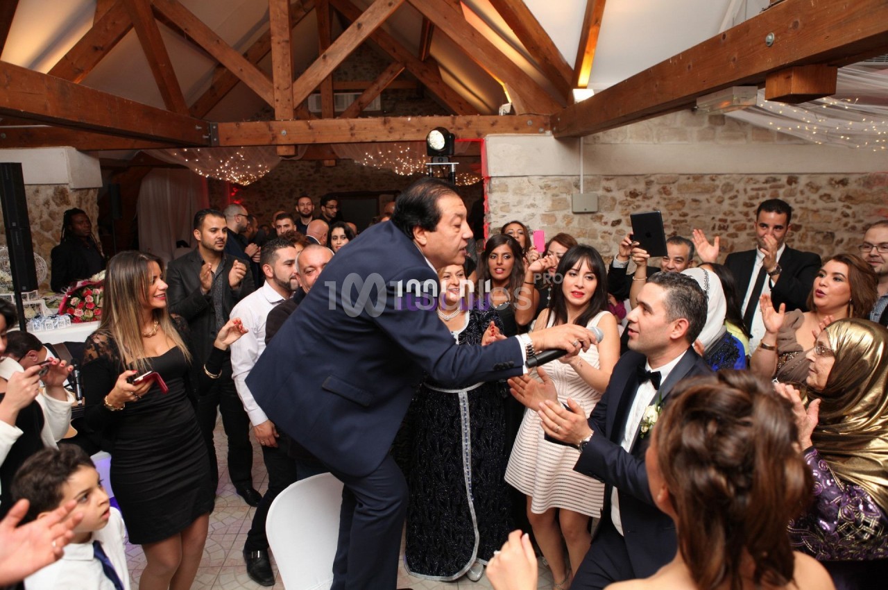 Un homme chante avec un micro au milieu d'une foule lors d'une fête dans une salle avec poutres apparentes.