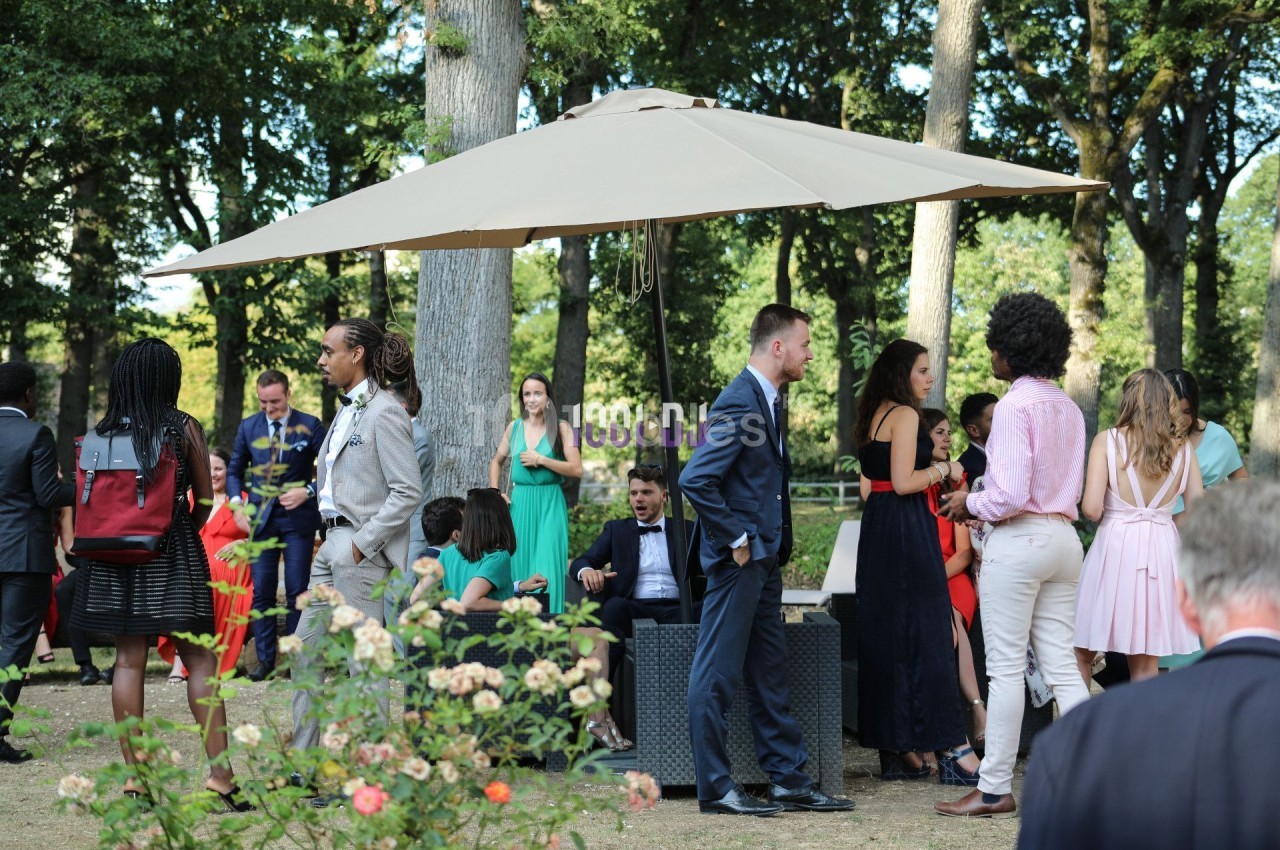 Des personnes discutent et se détendent sous un grand parasol dans un jardin entouré d'arbres et de fleurs.