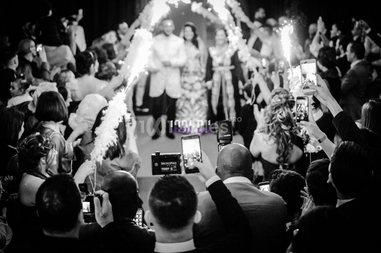 Des mariés avancent sous des étincelles tenues par des invités, entourés d'une foule prenant des photos.