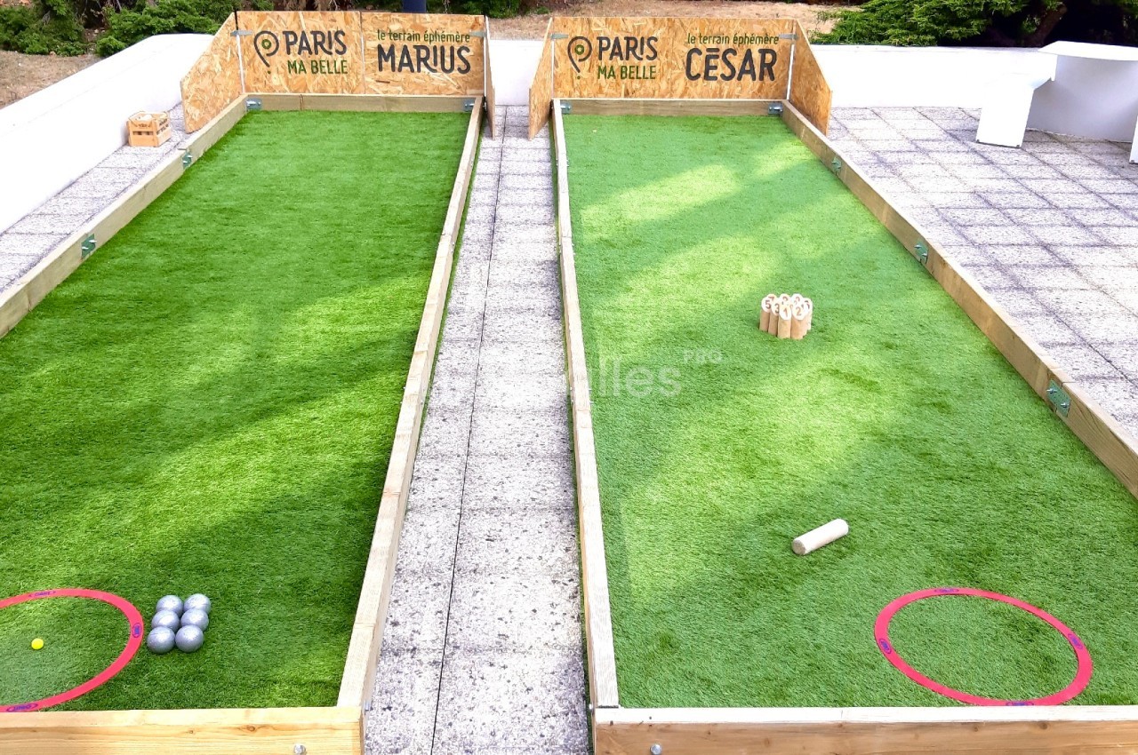 Deux terrains de pétanque en gazon synthétique avec boules et quilles, entourés d'une terrasse carrelée.