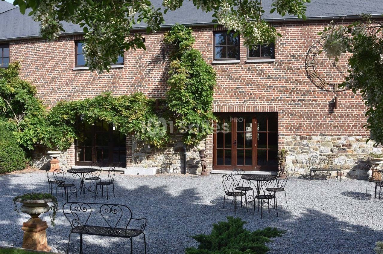 Façade en briques d'une maison avec des plantes grimpantes, terrasse en gravier et mobilier de jardin en fer forgé.
