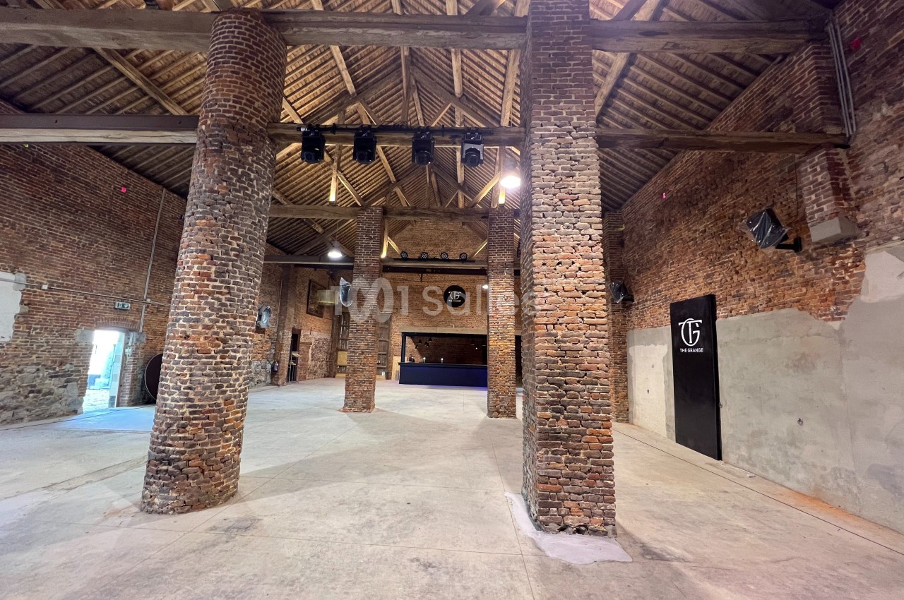 Intérieur d'une grande salle en briques avec poutres apparentes, colonnes en briques et espace ouvert.