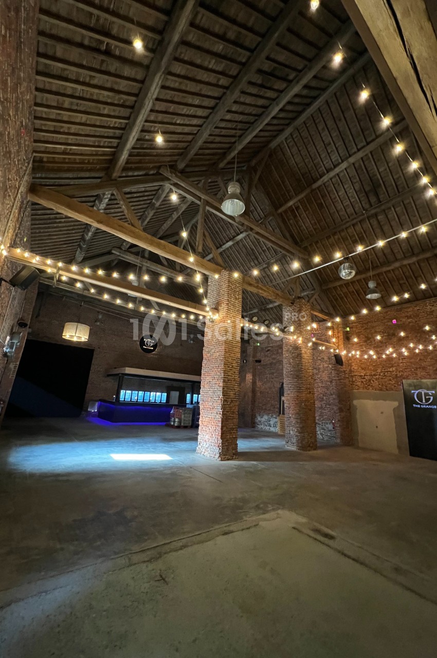 Intérieur d'un bâtiment en briques avec plafond en bois, éclairé par des guirlandes lumineuses suspendues.
