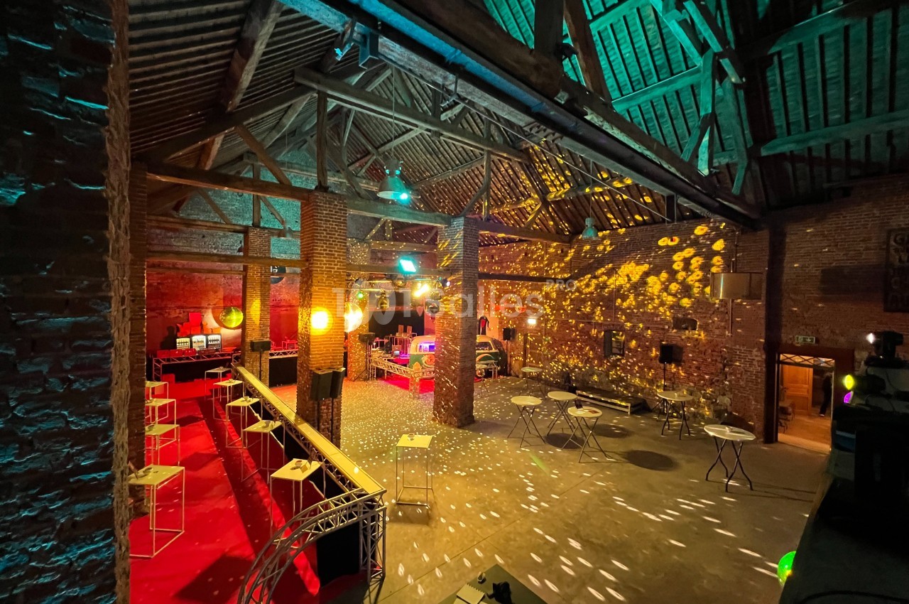 Salle en briques avec poutres apparentes, éclairée par des lumières colorées et des reflets de boule disco.