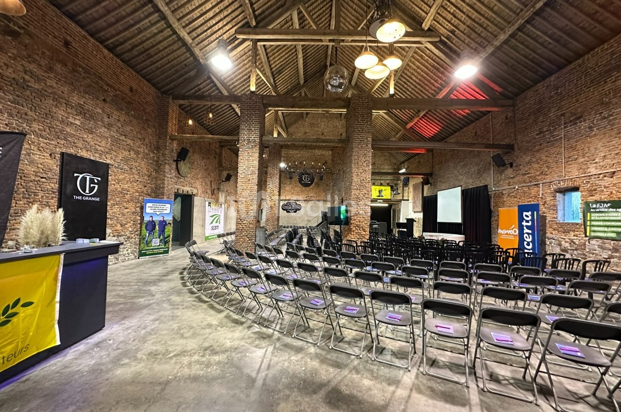 Salle en briques avec des rangées de chaises alignées, un bar à gauche et des écrans de projection à l’arrière.