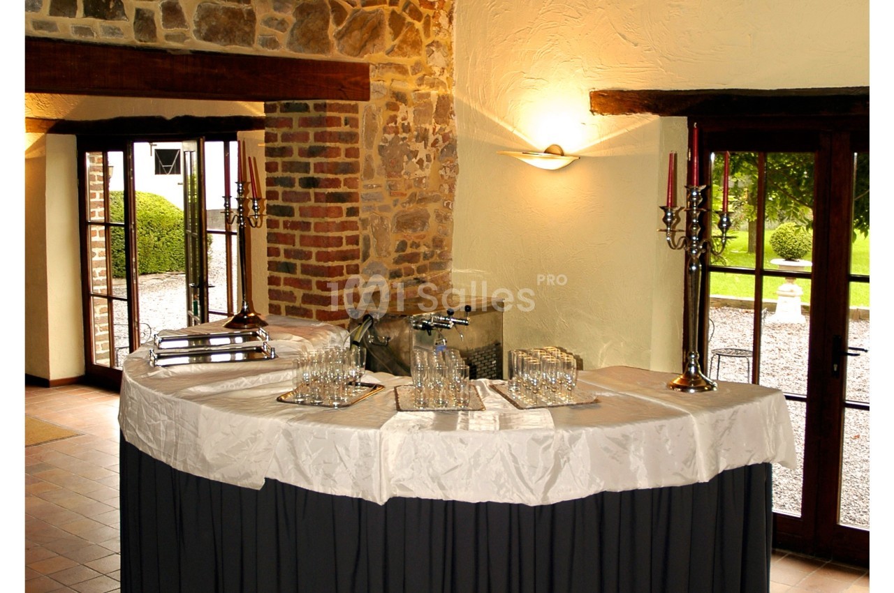 Table de réception avec nappes blanches, verres disposés et chandeliers, dans une salle au mur en pierre et ouvertures…