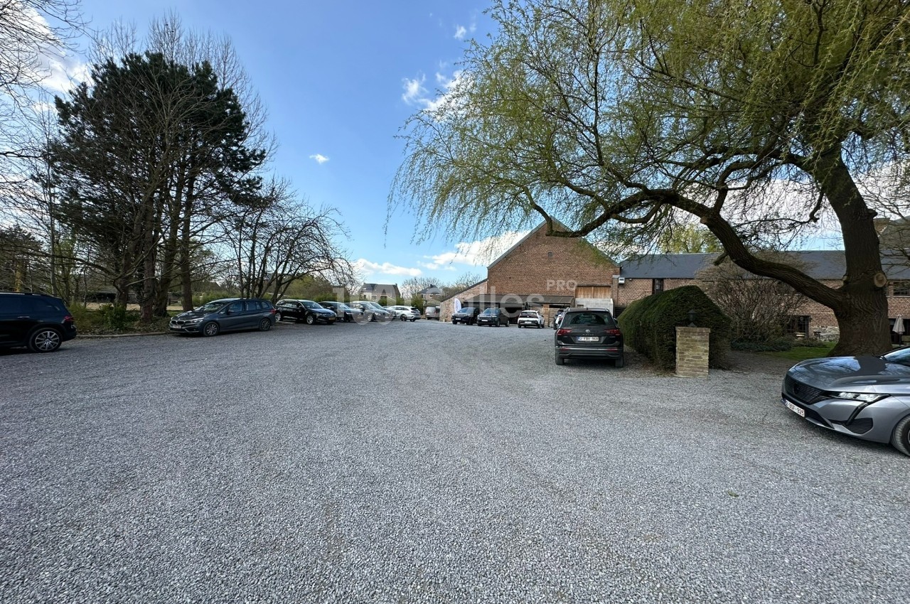 Parking en gravier entouré d'arbres et de bâtiments en briques sous un ciel partiellement nuageux.