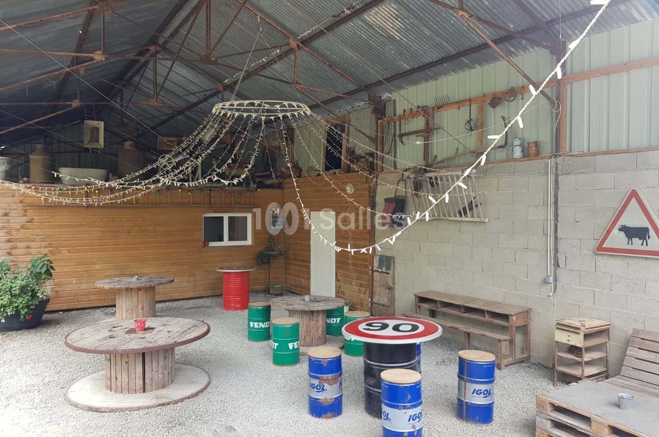 Espace extérieur couvert avec tables en tonneaux, guirlandes lumineuses et décorations rustiques.