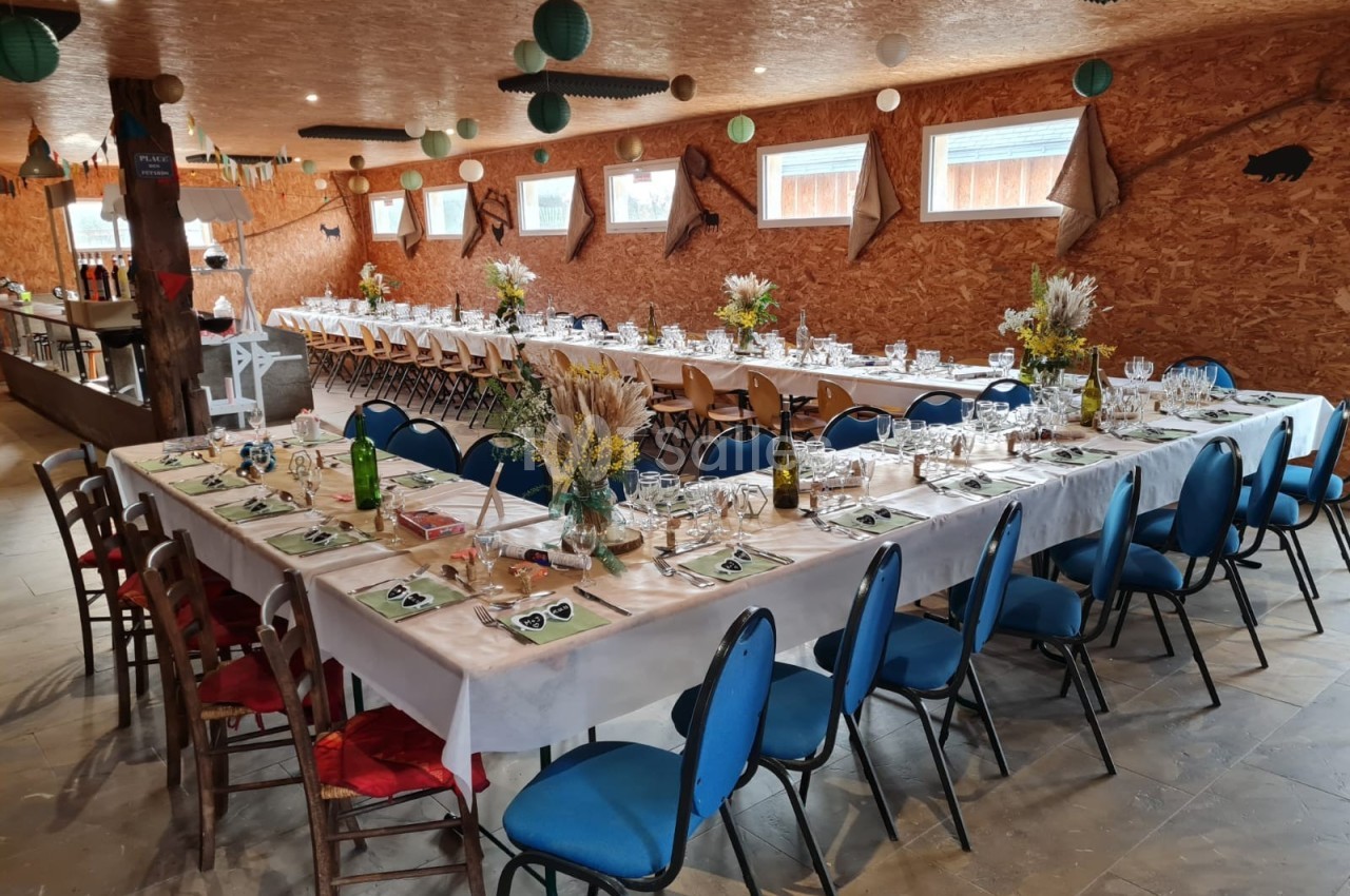 Salle décorée pour un repas avec de longues tables dressées, chaises colorées et arrangements floraux champêtres.