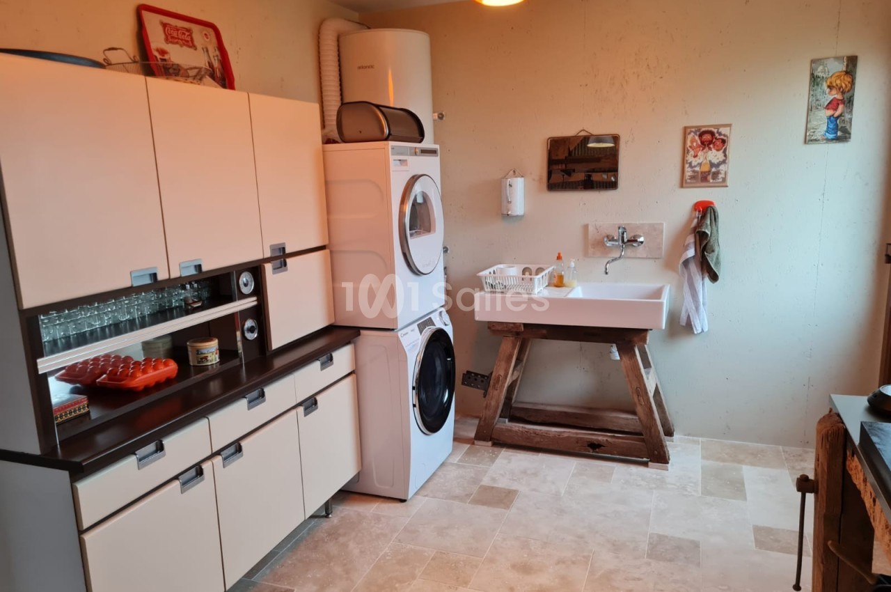 Buanderie avec lave-linge, sèche-linge empilés, évier sur pied en bois, meubles de rangement et décoration murale.