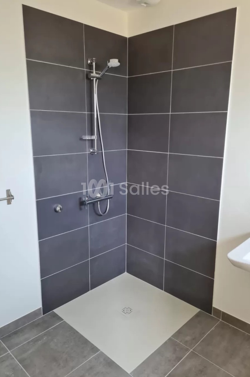 Douche à l'italienne avec carrelage gris foncé, receveur blanc et robinetterie murale en acier inoxydable.