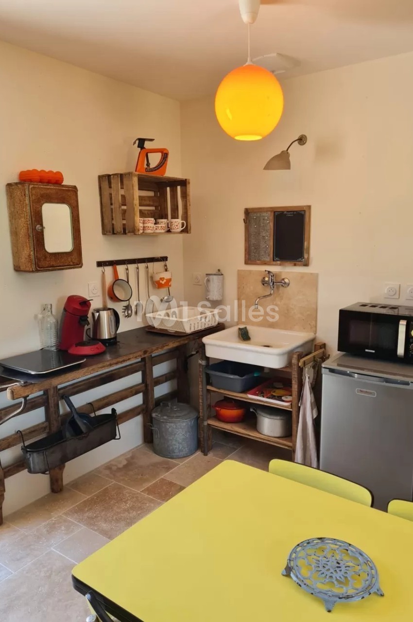 Petite cuisine équipée avec évier, micro-ondes, cafetière, étagères en bois et table jaune.
