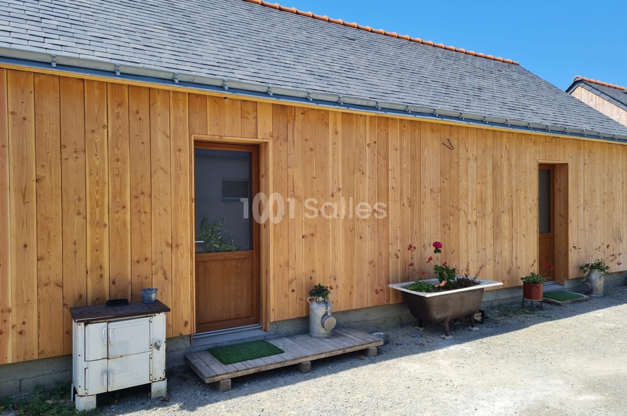 Façade en bois d'une maison avec deux portes, des plantes en pots et une baignoire ancienne en extérieur.