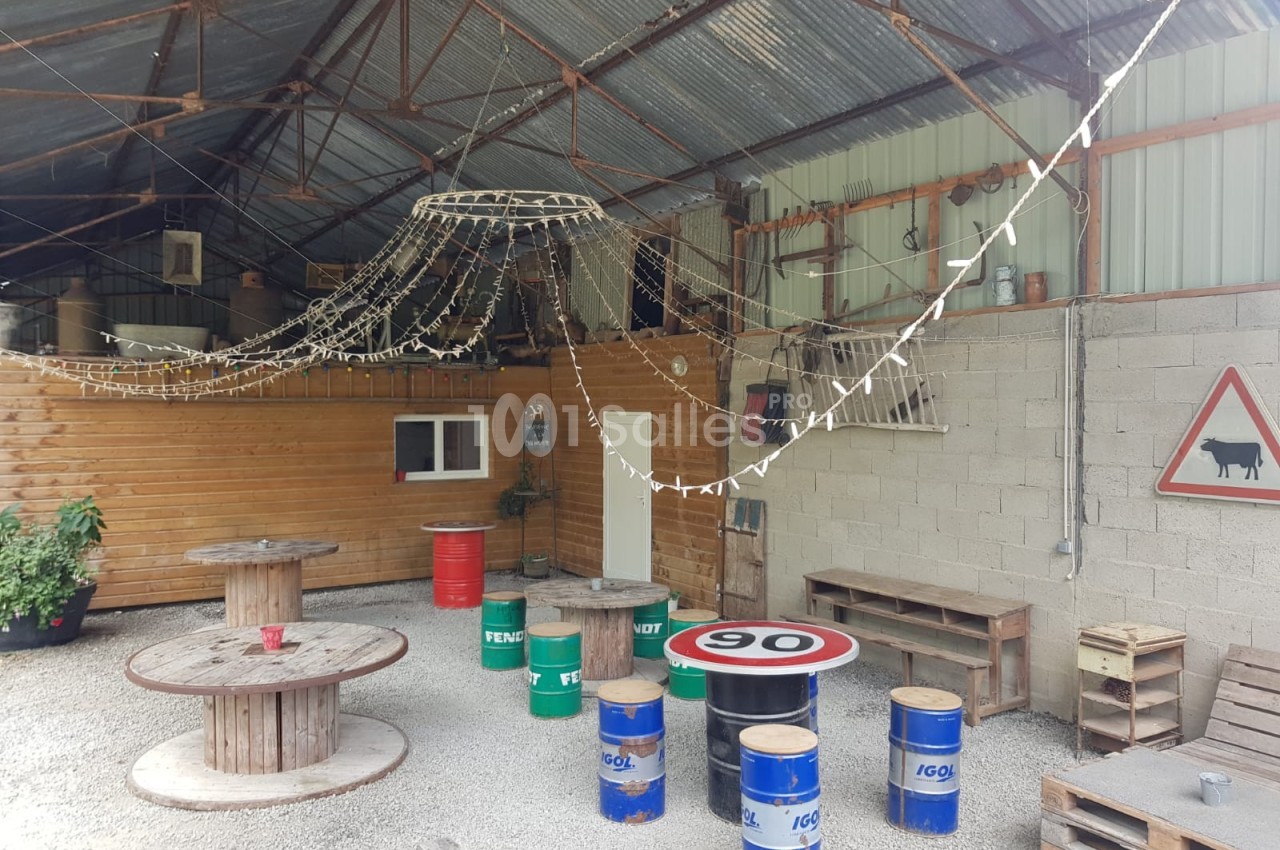 Espace couvert avec tables faites de tonneaux, guirlandes lumineuses suspendues et panneaux décoratifs sur les murs.
