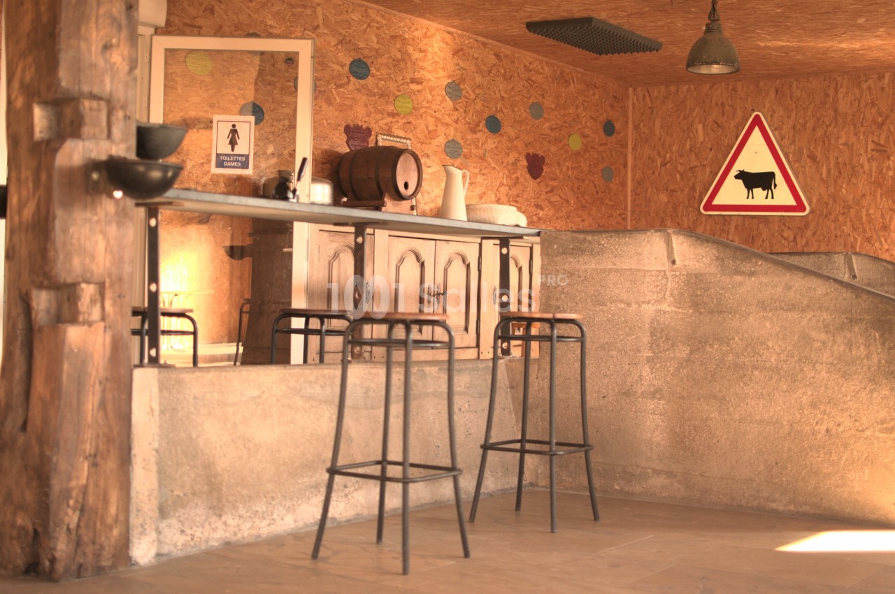 Intérieur rustique avec un bar en bois, tabourets hauts, mur en bois décoré et panneau de signalisation avec une vache.