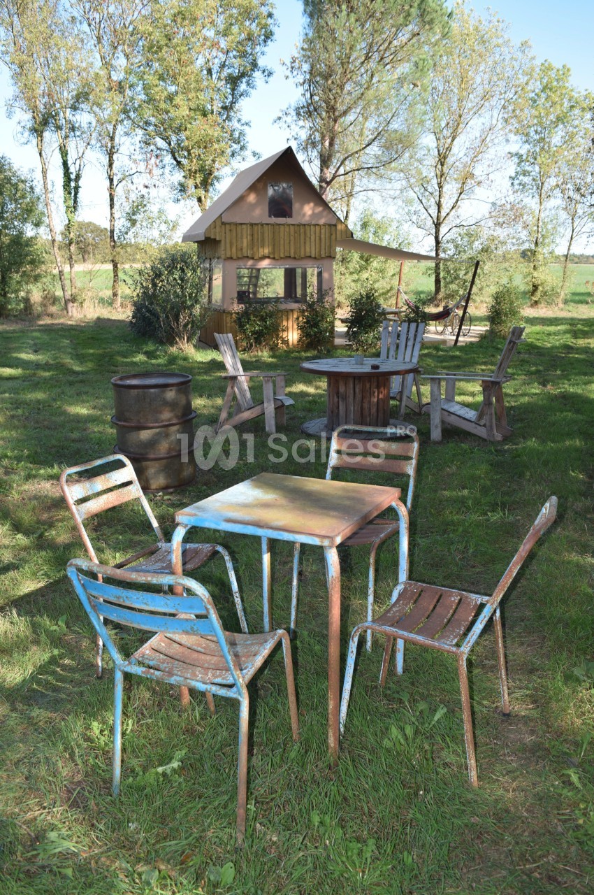 Mobilier de jardin en métal et bois disposé sur une pelouse, avec une cabane en arrière-plan entourée d'arbres.