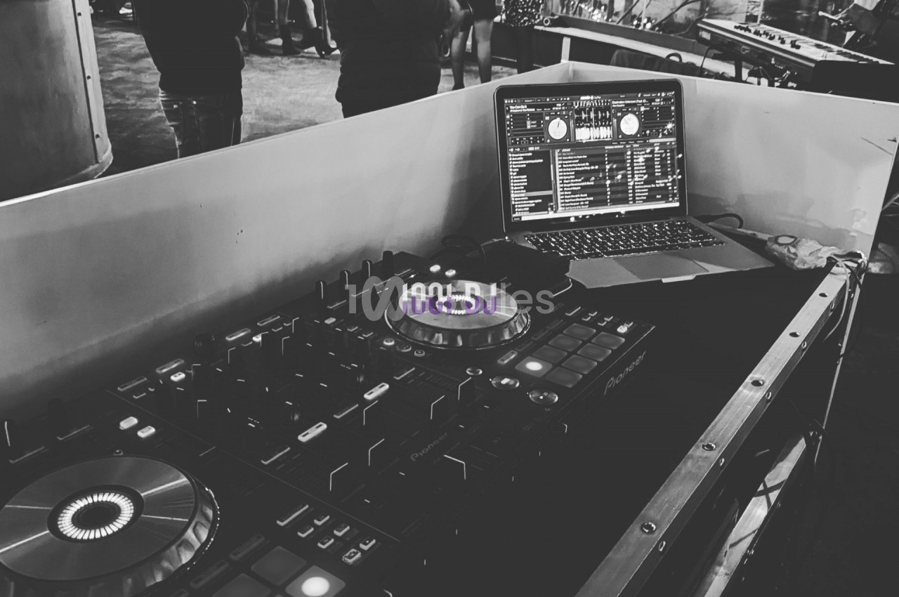 Console de DJ avec platines et ordinateur portable dans un espace animé, éclairé par des lumières urbaines.
