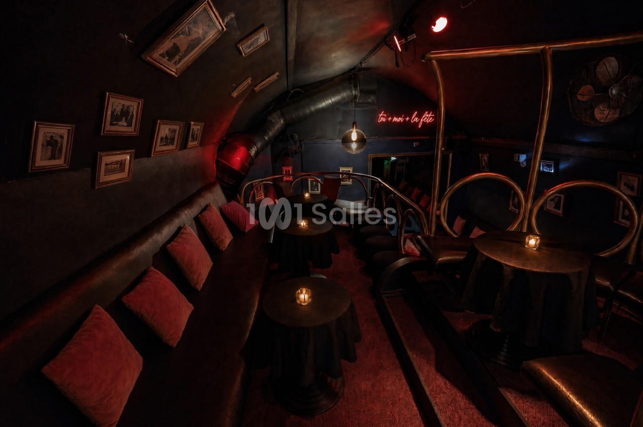 Salle sombre avec banquettes, petites tables éclairées par des bougies, décorations murales et lumière tamisée.