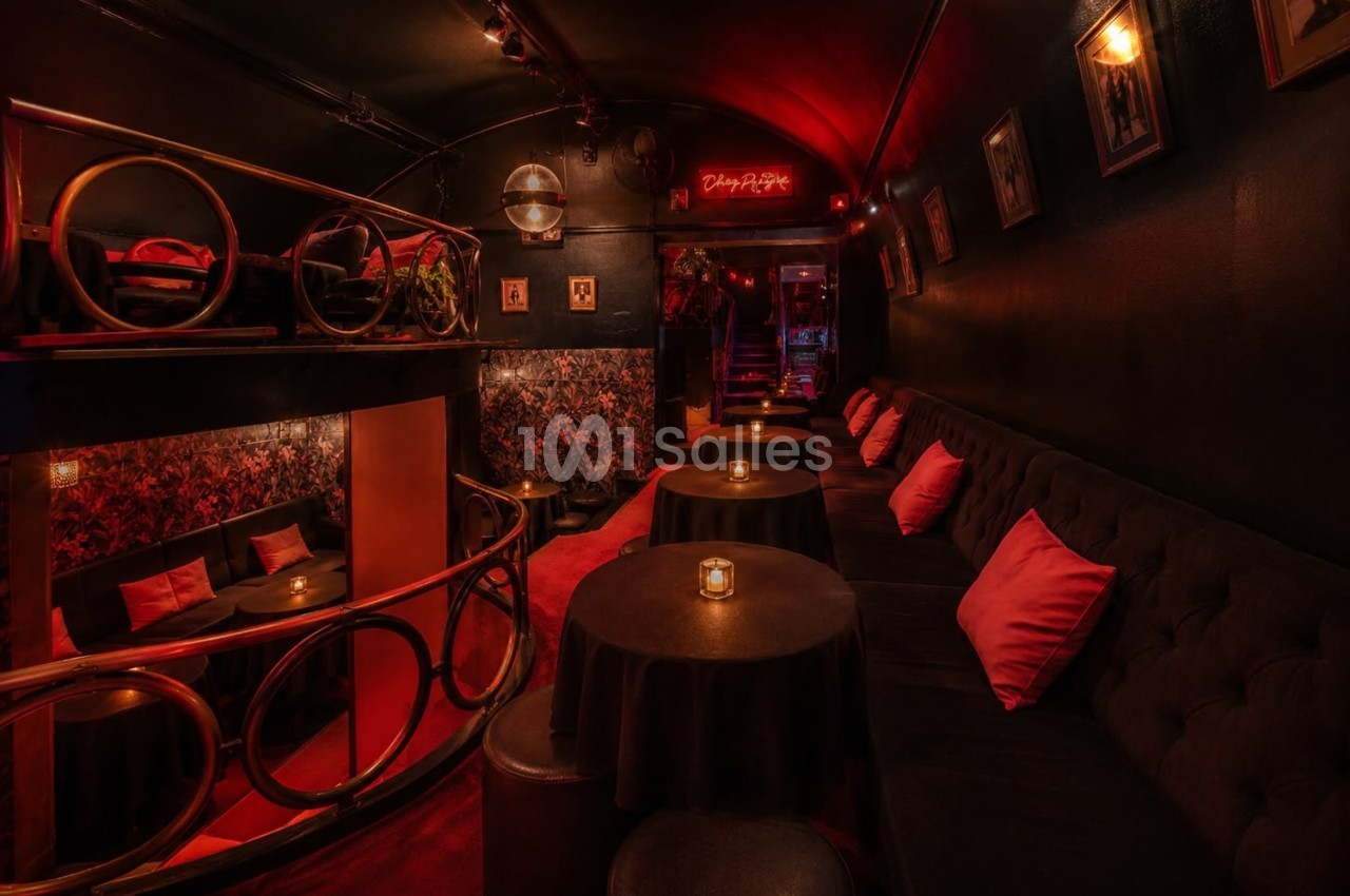 Salle intimiste avec éclairage tamisé, banquettes noires, coussins rouges et petites tables éclairées par des bougies.