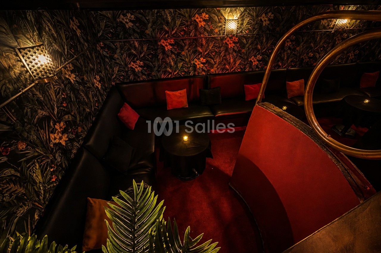 Banquette en cuir noir entourant des tables basses dans un espace sombre, décoré de motifs floraux et éclairé doucement.