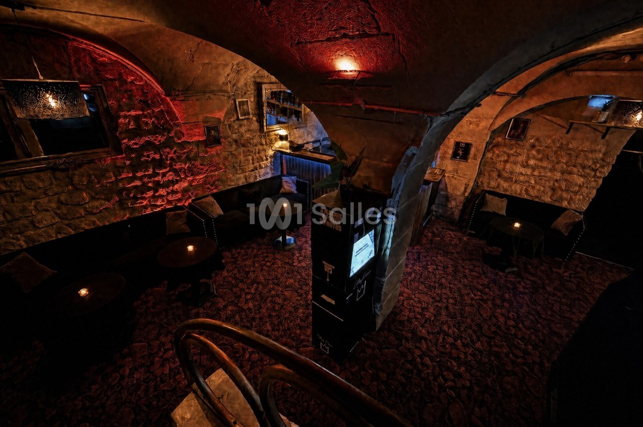 Salle voûtée en pierre avec éclairage tamisé, tables rondes et ambiance chaleureuse.