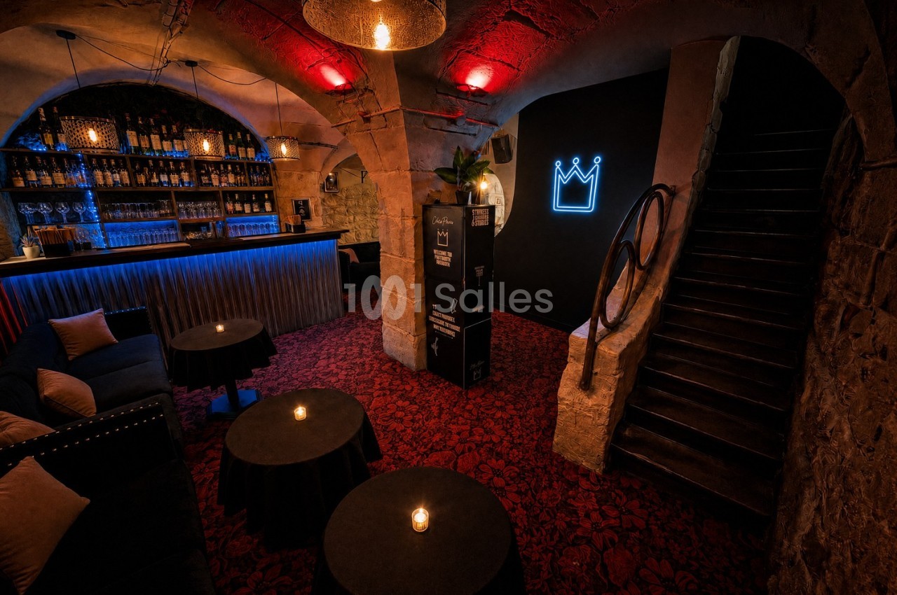 Salle voûtée avec bar éclairé, tables basses et fauteuils, éclairage tamisé et enseigne lumineuse en forme de couronne.