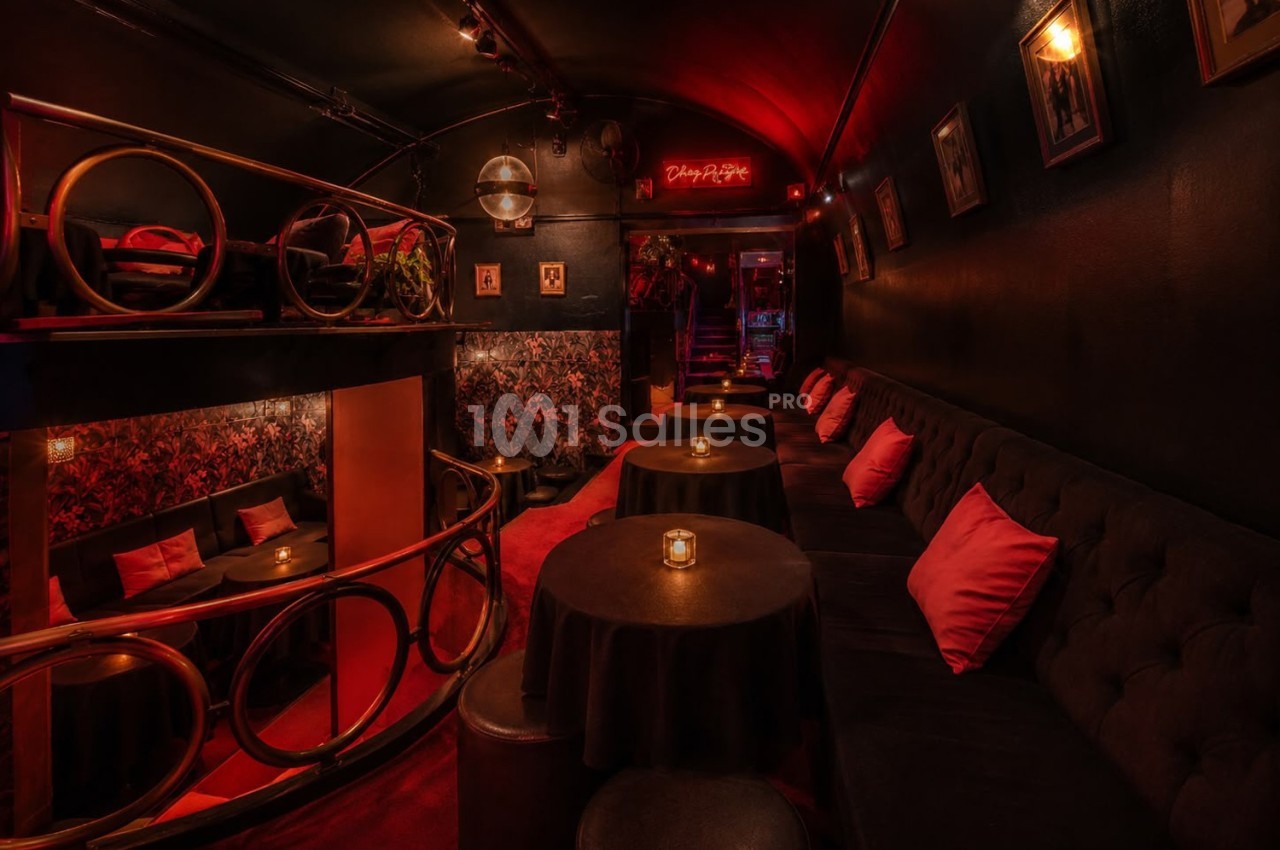 Salle intimiste avec éclairage tamisé, banquettes noires, coussins rouges et petites tables éclairées par des bougies.