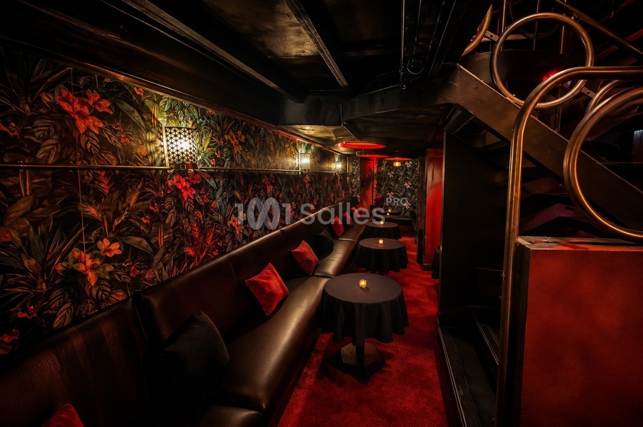 Banquette en cuir noir, tables rondes et décor mural floral dans un espace intérieur à l'éclairage tamisé.