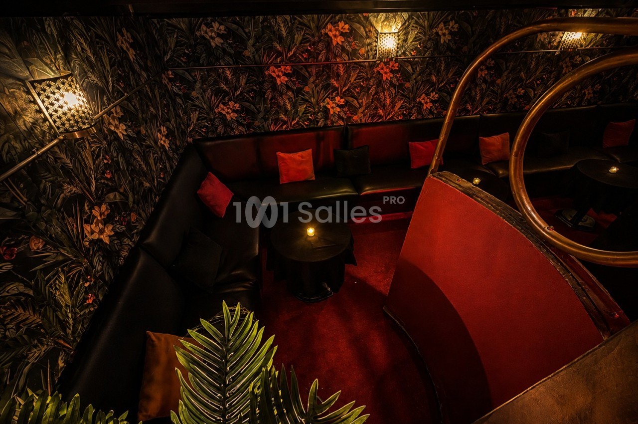 Banquette en cuir noir entourant des tables basses dans un espace sombre, décoré de motifs floraux et éclairé doucement.