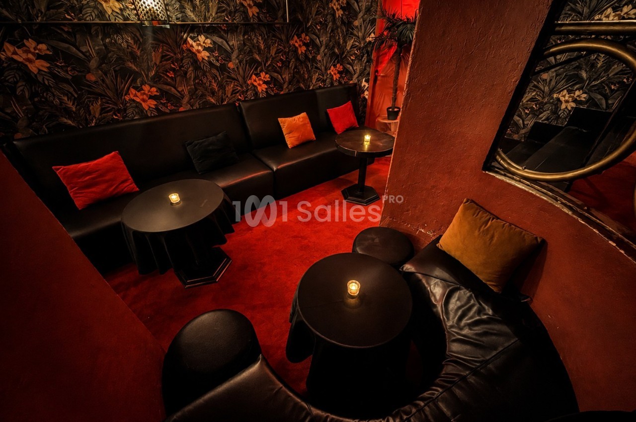 Salon intime avec canapés noirs, tables basses rondes, bougies allumées et murs ornés de motifs végétaux.