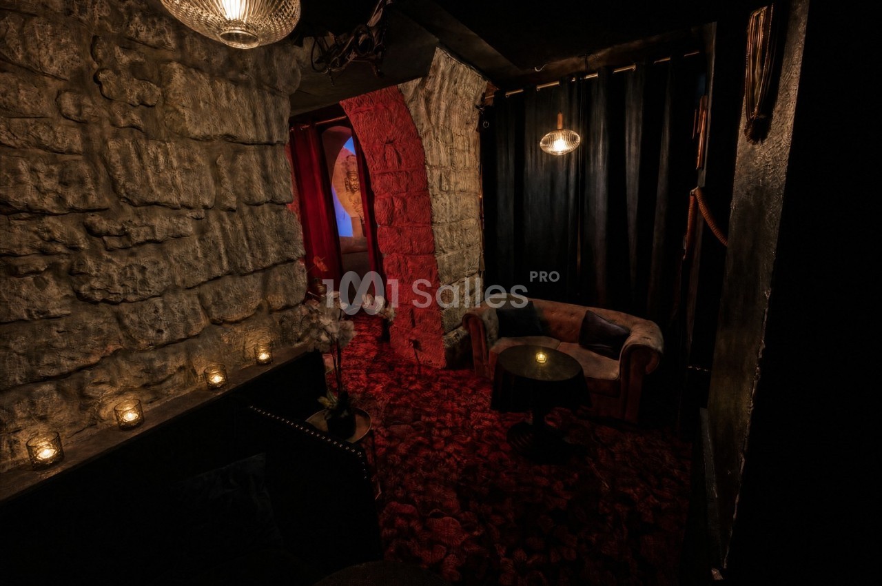 Salon intimiste avec murs en pierre, éclairage tamisé, canapé, table basse et rideaux sombres.