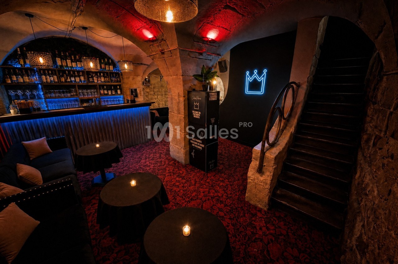 Salle voûtée avec bar éclairé, tables basses et fauteuils, éclairage tamisé et enseigne lumineuse en forme de couronne.