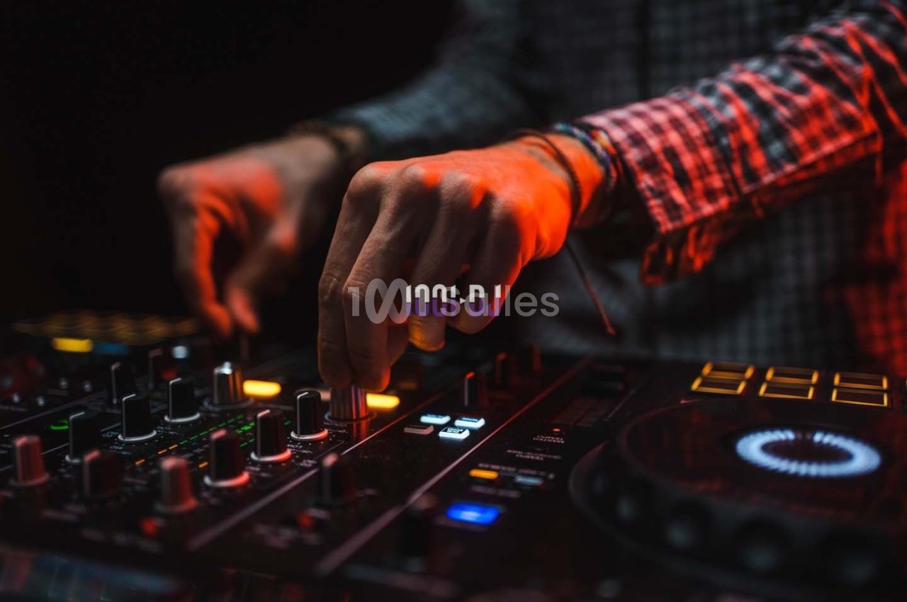 Main ajustant des commandes sur une table de mixage DJ illuminée par des lumières rouges et oranges.