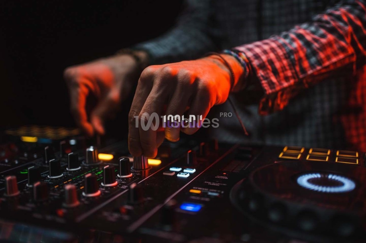 Main ajustant des commandes sur une table de mixage DJ illuminée par des lumières rouges et oranges.