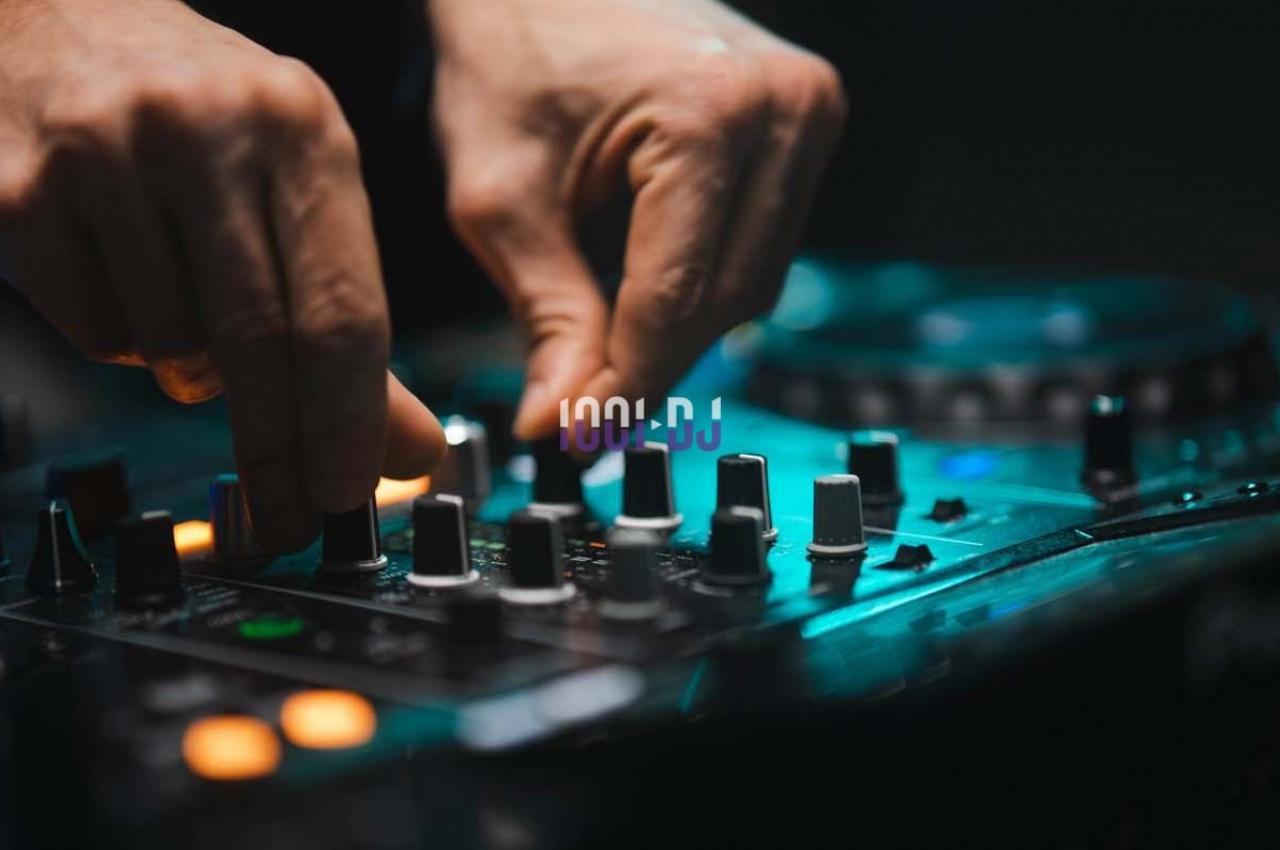 Mains ajustant les réglages sur une table de mixage audio éclairée dans un environnement sombre.