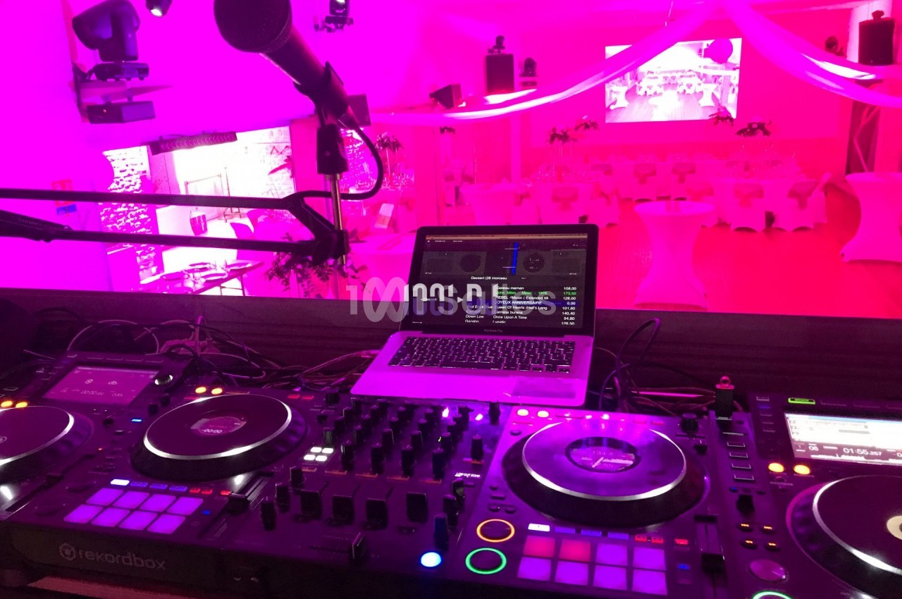 Table de mixage DJ avec platines, microphone et ordinateur portable dans une salle éclairée par des lumières roses.