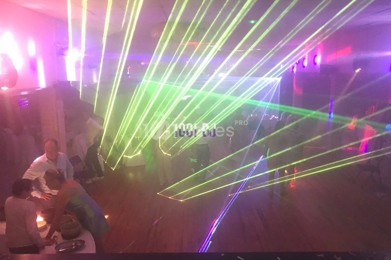 Des faisceaux laser colorés illuminent une salle sombre où des personnes discutent et se déplacent.
