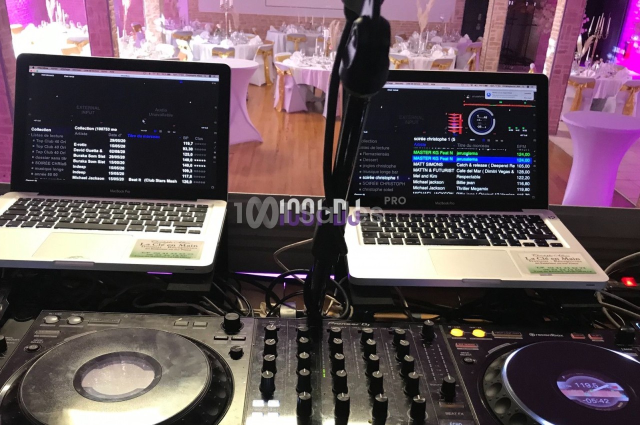 Deux ordinateurs portables et une console de mixage installés pour une prestation DJ dans une salle de réception décorée.