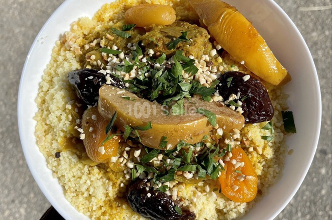 Assiette de couscous garnie de légumes, fruits secs, viande et herbes fraîches, servie sur une table en extérieur.