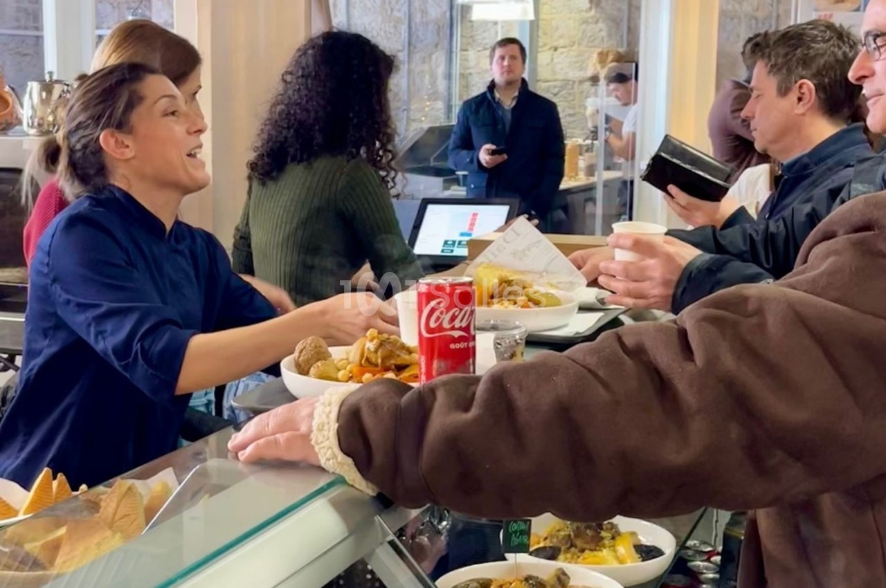 Une employée sert des clients à un comptoir de restaurant, avec des plats et une canette de soda visibles.