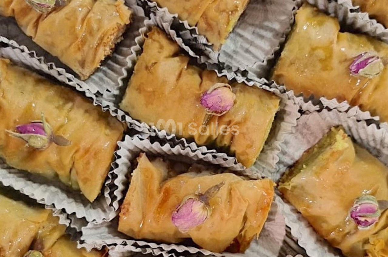 Pâtisseries baklavas dorées garnies de pétales de rose, présentées dans des caissettes en papier.