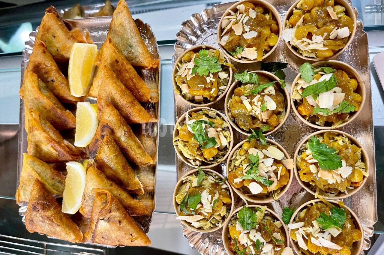 Assortiment de samoussas dorés avec des quartiers de citron et petits bols garnis de fruits secs et herbes fraîches.