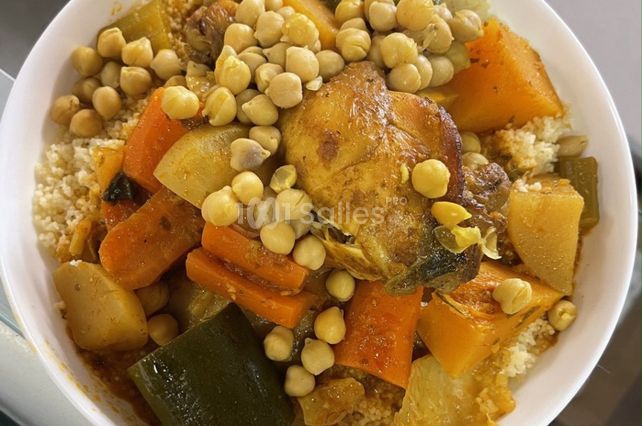 Plat de couscous garni de légumes variés, pois chiches et morceaux de viande dans un bol blanc.