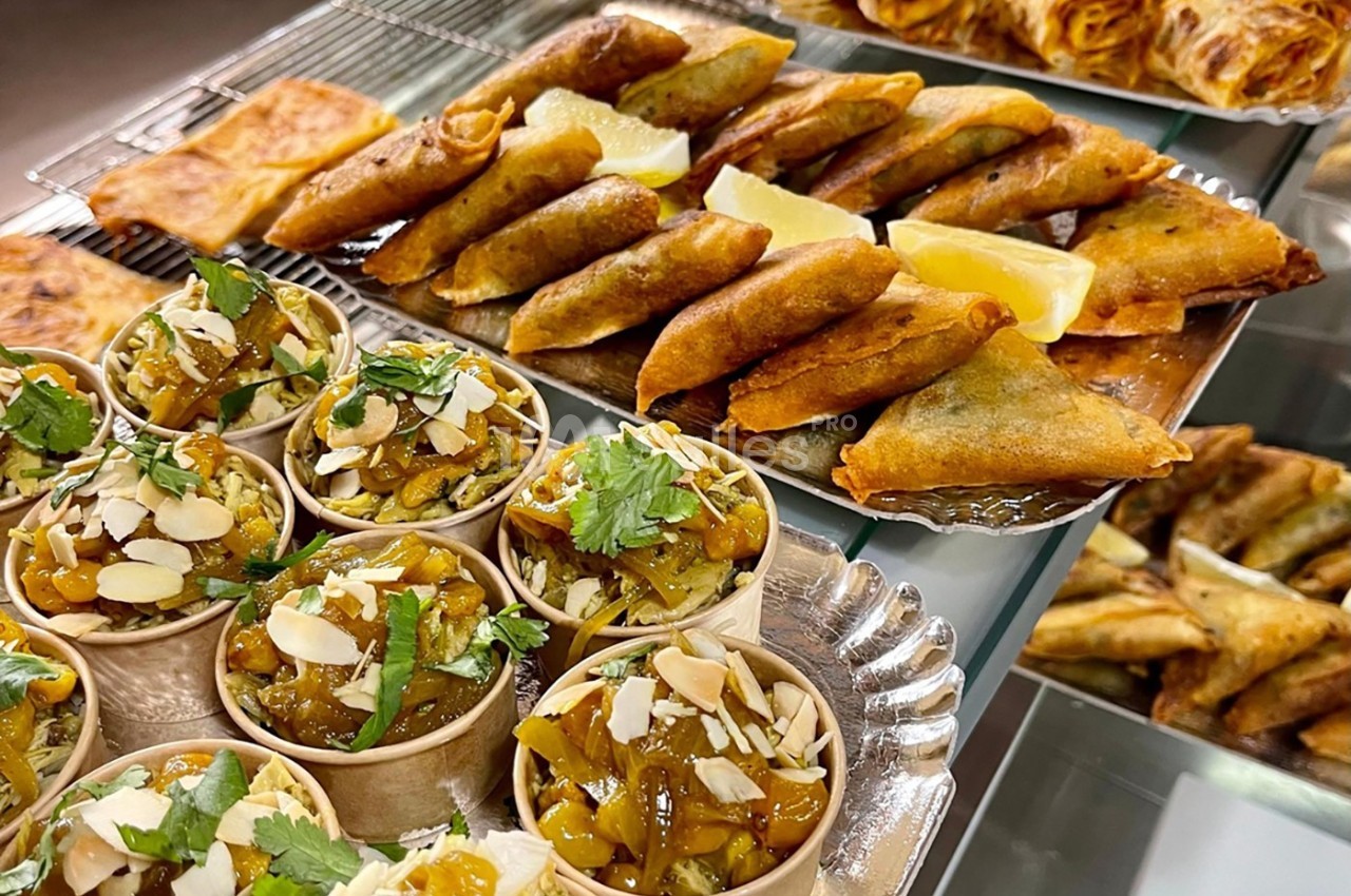 Assortiment de samoussas dorés, crêpes farcies et verrines garnies de légumes et amandes, décorées de coriandre.