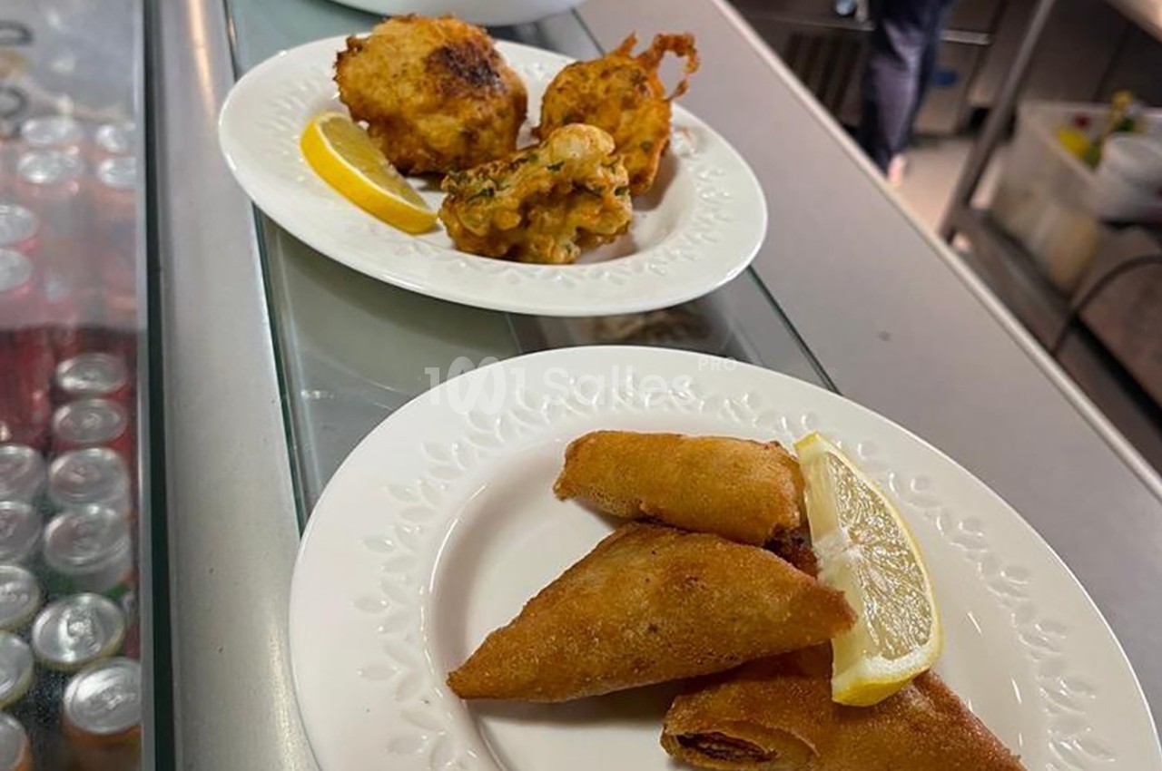 Assiette contenant des samoussas dorés avec un quartier de citron, posée sur un comptoir près d'une autre assiette de…