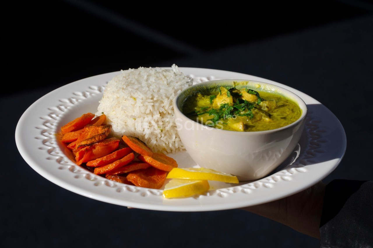 Assiette contenant du riz blanc, des carottes rôties et un bol de curry jaune garni de coriandre, avec des tranches de…