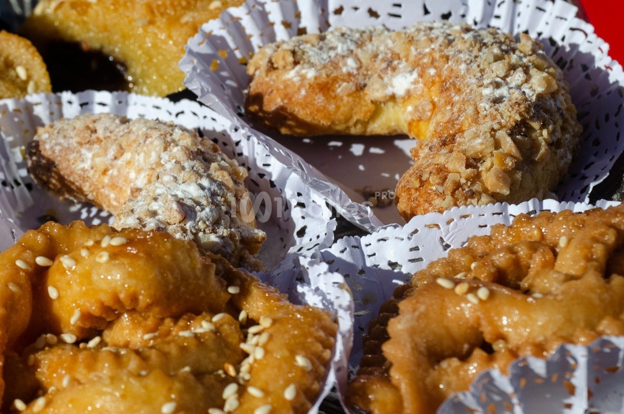 Pâtisseries traditionnelles garnies de sucre glace et de graines de sésame, présentées sur des napperons en papier.