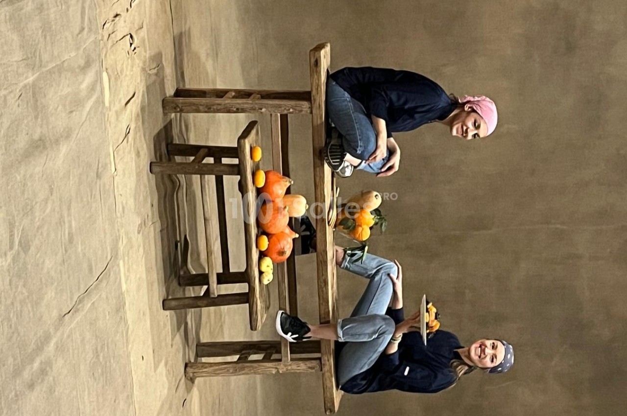 Deux personnes assises à une table en bois avec des courges et des fruits disposés autour.