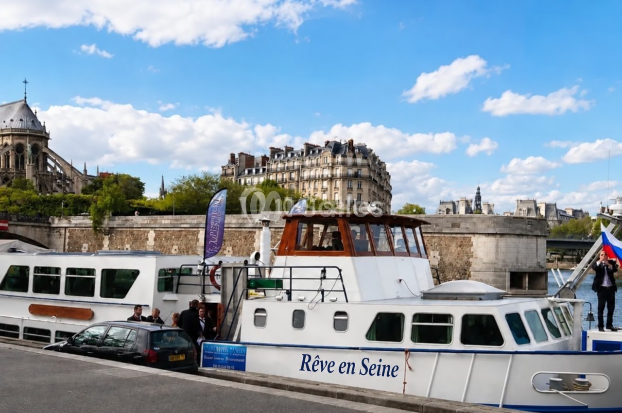 Bateau de croisière amarré sur la Seine à Paris, avec des passagers montant à bord et des bâtiments en arrière-plan.